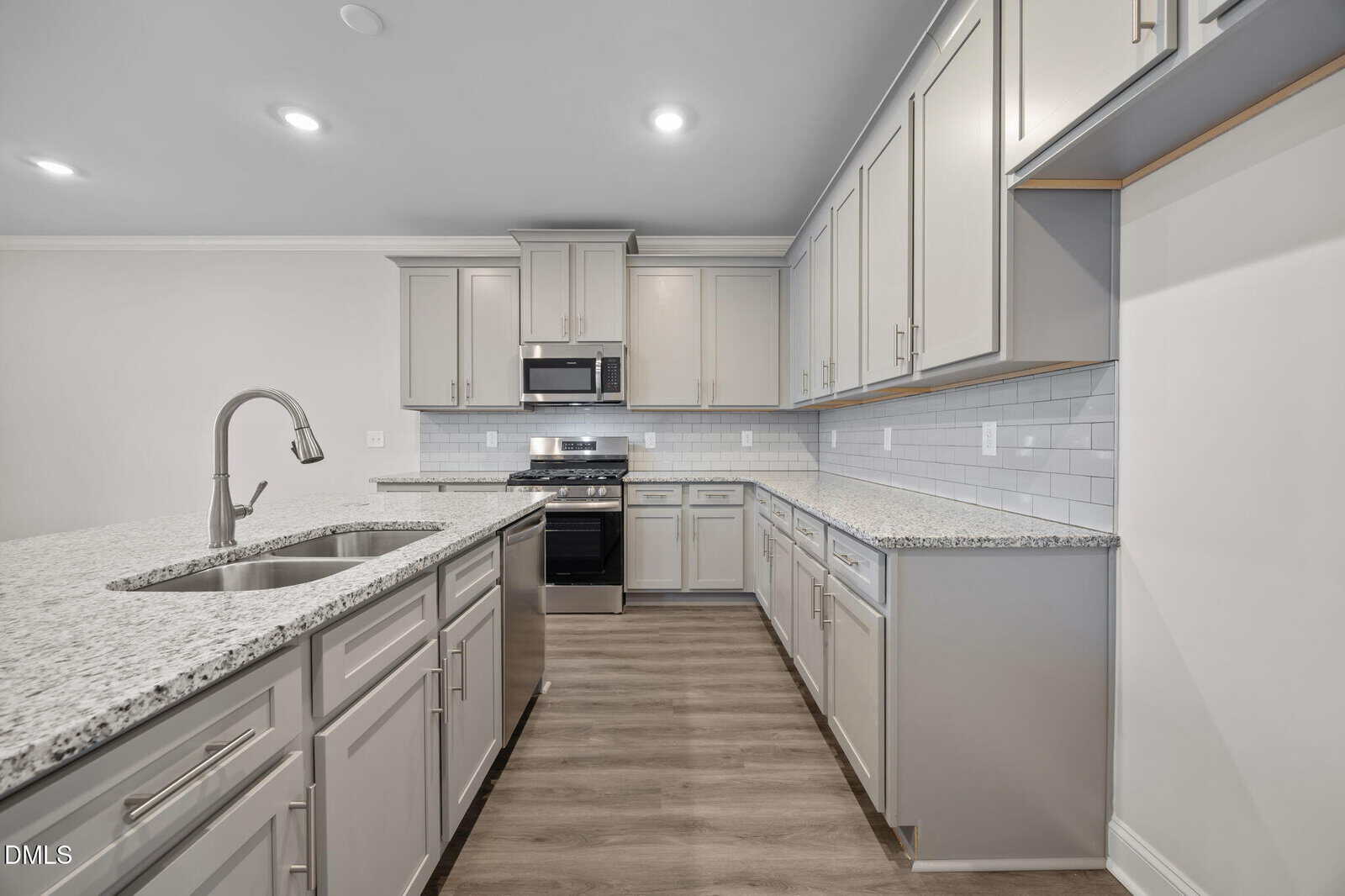 Modern kitchen with light gray cabinets, granite countertops, stainless steel appliances, a gas stove, built-in microwave, double sink with gooseneck faucet, white subway tile backsplash, and wood-look flooring.