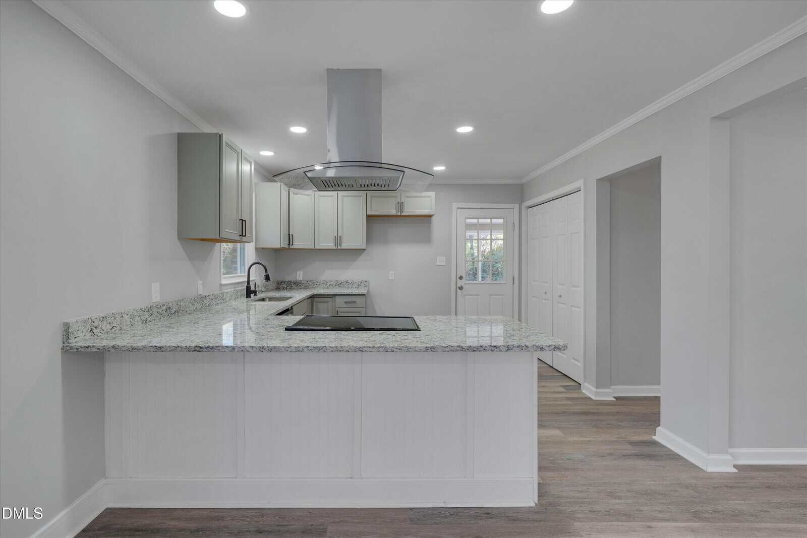 Modern kitchen with light gray cabinets, a granite countertop peninsula, stainless steel range hood, electric cooktop, built-in sink, white walls, wood-style flooring, and recessed ceiling lights.