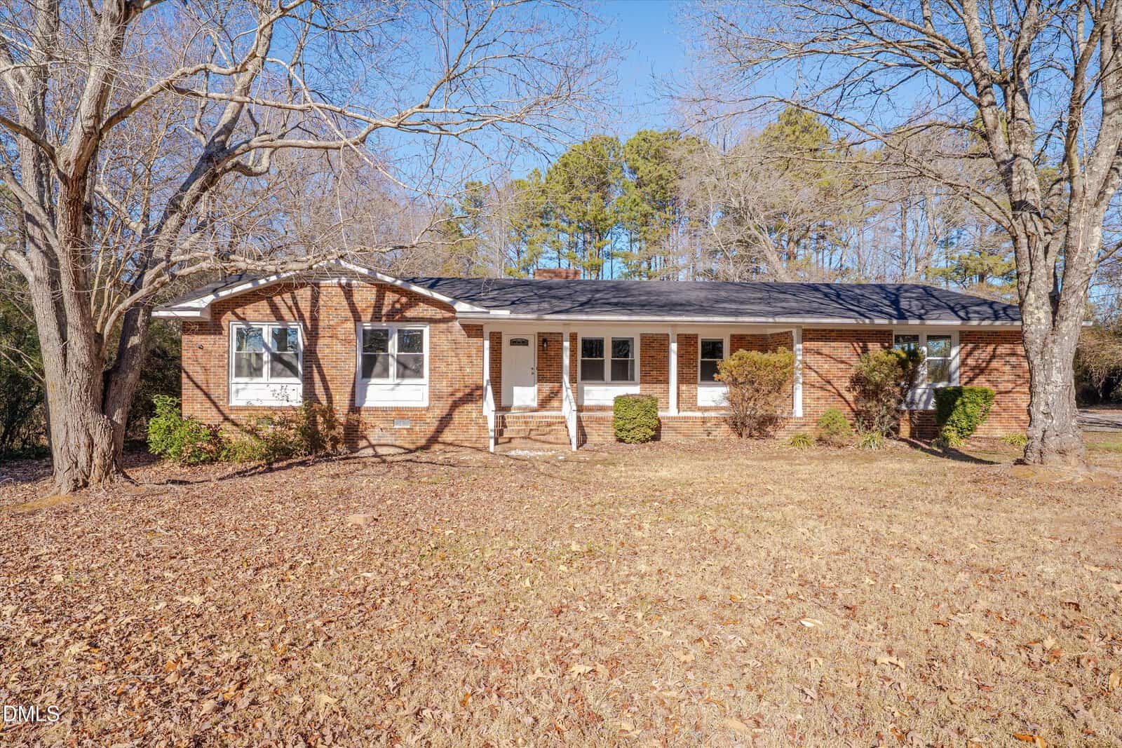 Charming single-story brick house at 2728 S Cokesbury Road in Henderson, featuring white trim, a dark shingle roof, and multiple windows. The yard has dry grass, scattered leaves, and several leafless trees beneath a clear blue sky.
