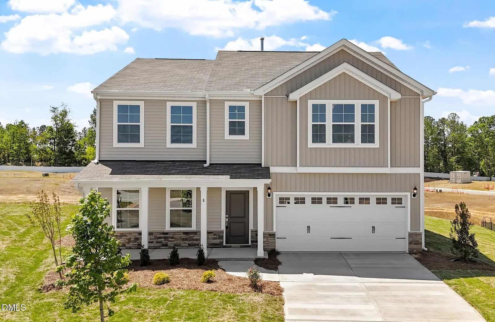 A two-story suburban house at 8 Lotus Bend Way, Youngsville, with light beige siding, white trim, a covered front porch, and a two-car garage sits on a newly landscaped lawn under a bright blue sky with scattered clouds.