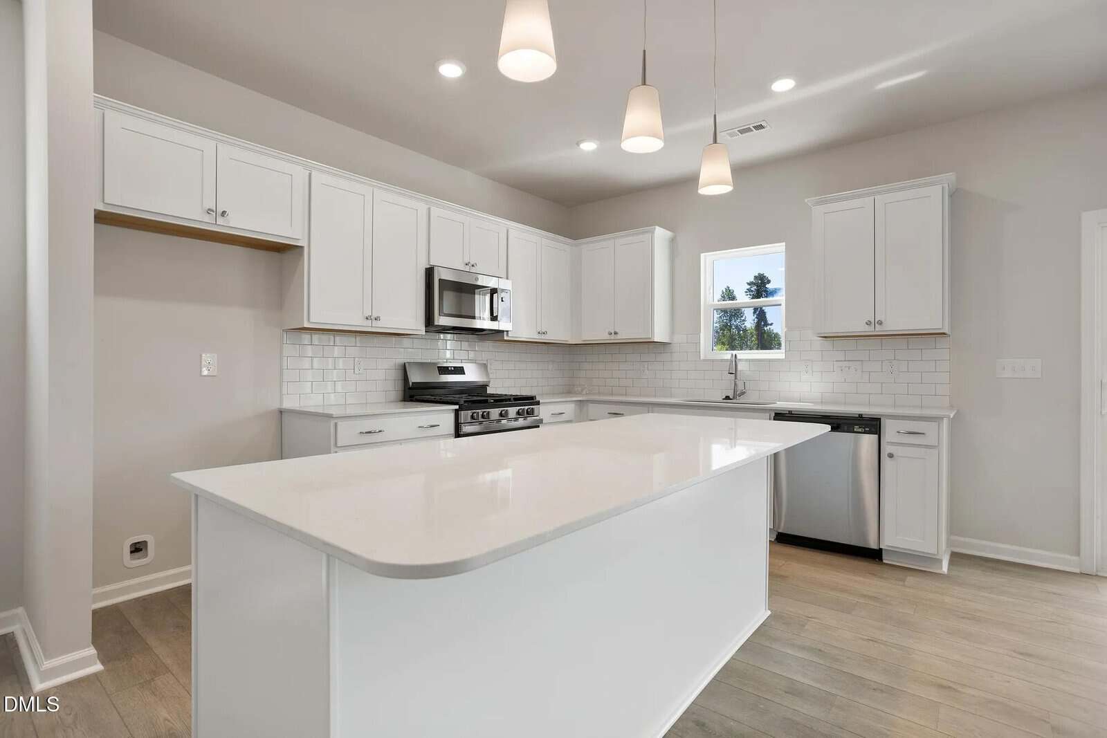 Modern kitchen with white cabinets, a large white island, stainless steel appliances, subway tile backsplash, light wood flooring, and three pendant lights hanging from the ceiling.