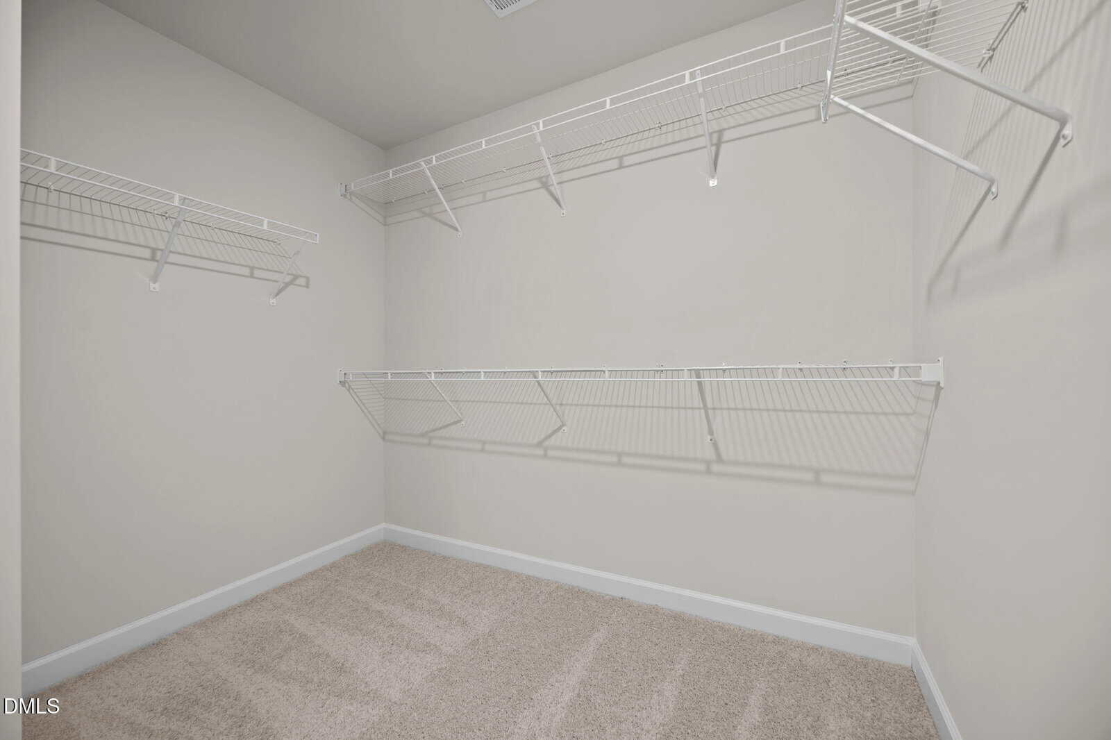 Empty walk-in closet with beige carpet, white walls, and multiple white wire shelves installed along two walls.
