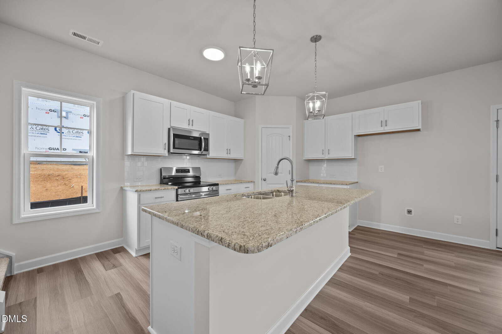 Modern kitchen with white cabinets, stainless steel appliances, a center island with sink, granite countertops, pendant lighting, light wood floors, and a window showing construction outside.