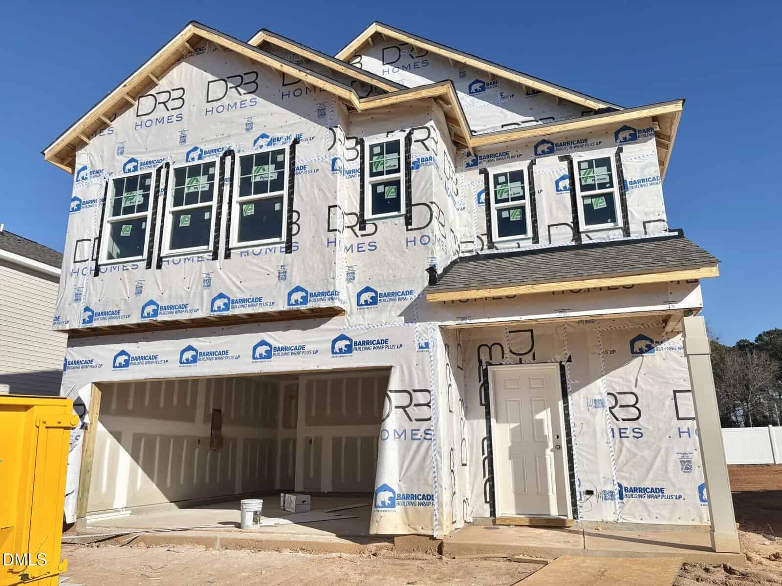 A two-story house under construction at 24 Gerrad Street in Franklinton, wrapped in white weatherproof material with visible logos. The open garage and unfinished exterior show progress; some windows are installed, and a yellow dumpster sits out front.
