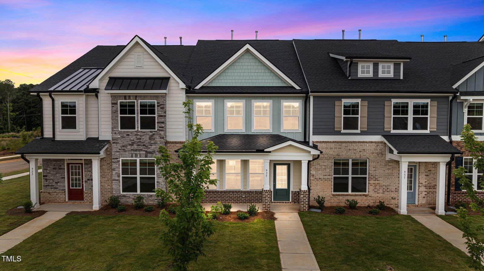 A row of modern townhouses at 935 Alma Railway Drive in Wake Forest features brick and siding exteriors, large windows, and small front yards, set against a vibrant sunset sky with purple, pink, and blue hues.
