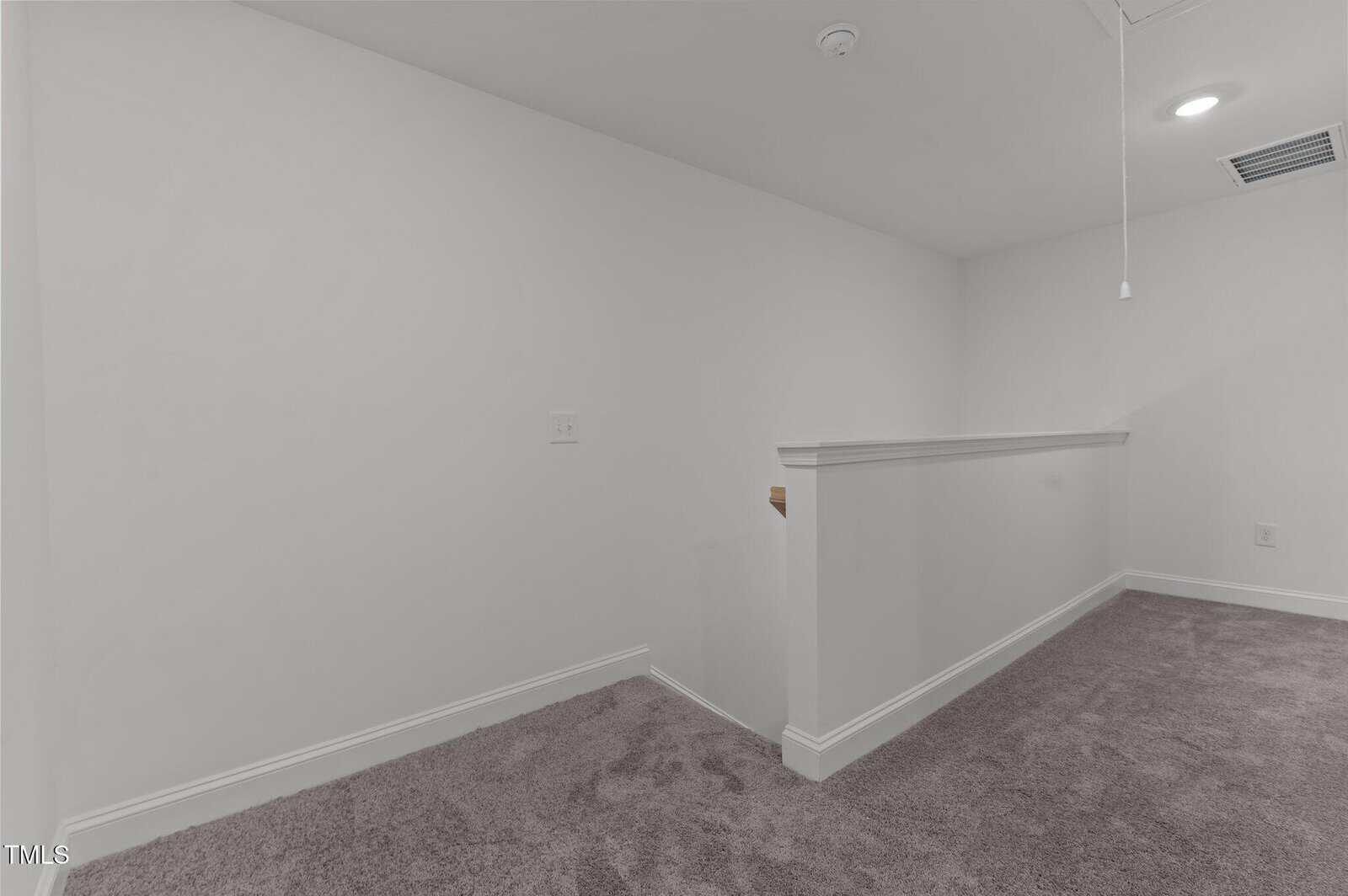 A small landing area with light gray walls, carpeted floor, and a half-wall railing. There is a ceiling vent, a smoke detector, a pull string, and a recessed light on the ceiling.