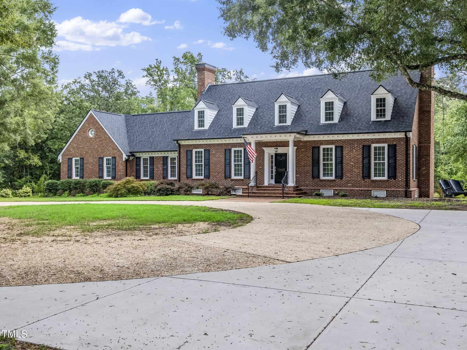 A large brick house with white trim, black shutters, multiple dormer windows, and an American flag by the front door sits at 270 Wiggins Road in Louisburg, surrounded by trees and a circular driveway in front.