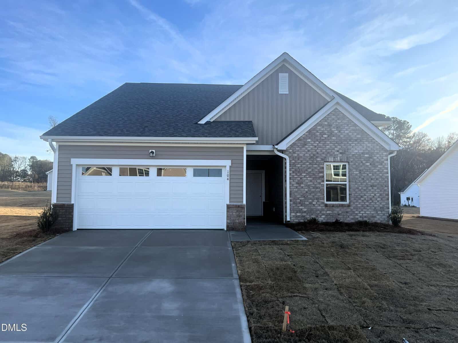 A newly built single-story house located at 104 Big Dream Court in Louisburg, featuring a brick and siding exterior, a two-car garage, and a covered entryway. The yard has fresh sod and the driveway is concrete. The sky is clear and blue.