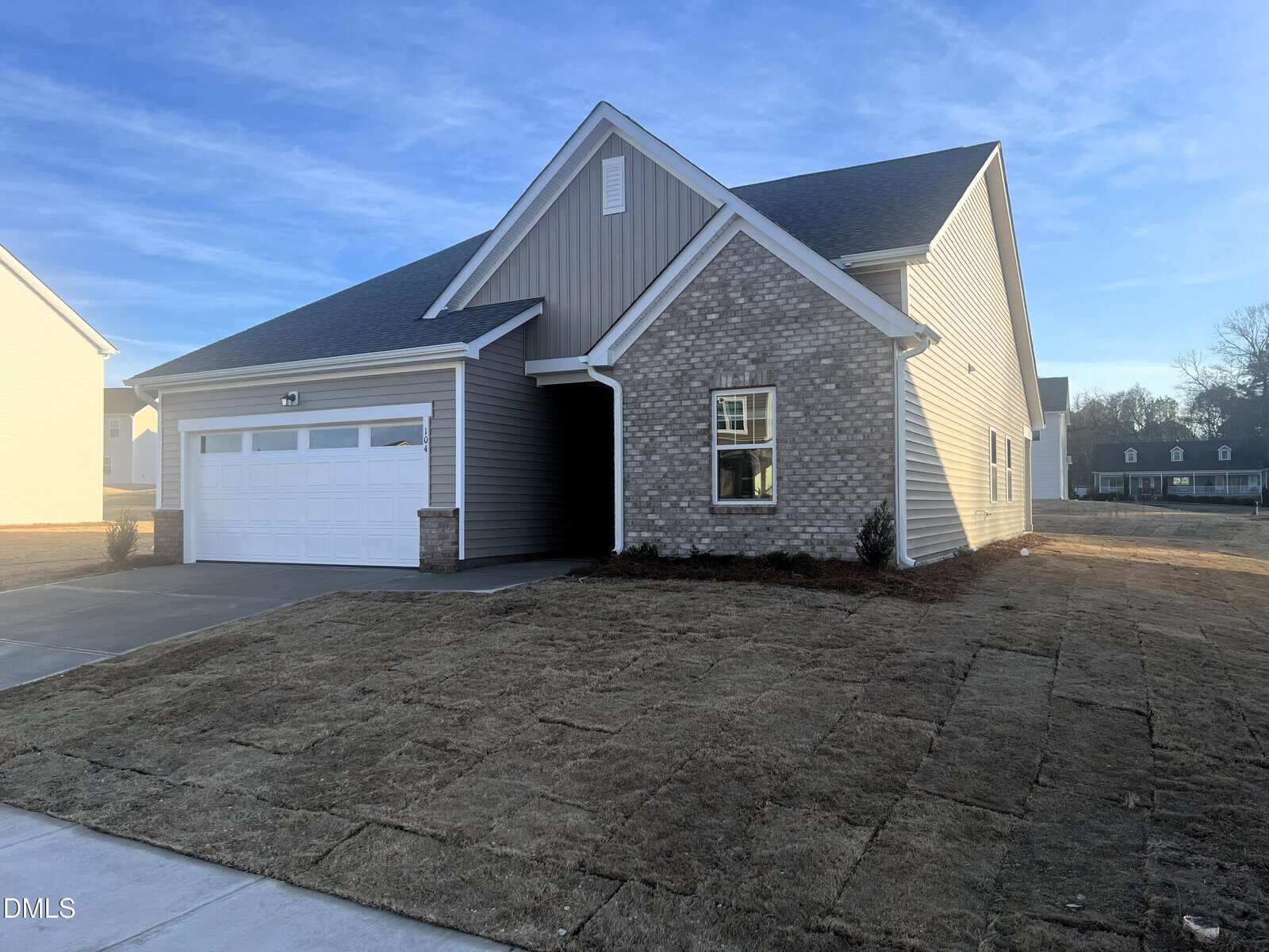 Single-story house with a gabled roof, two-car garage, brick and siding exterior, and newly laid sod in the front yard on a sunny day.