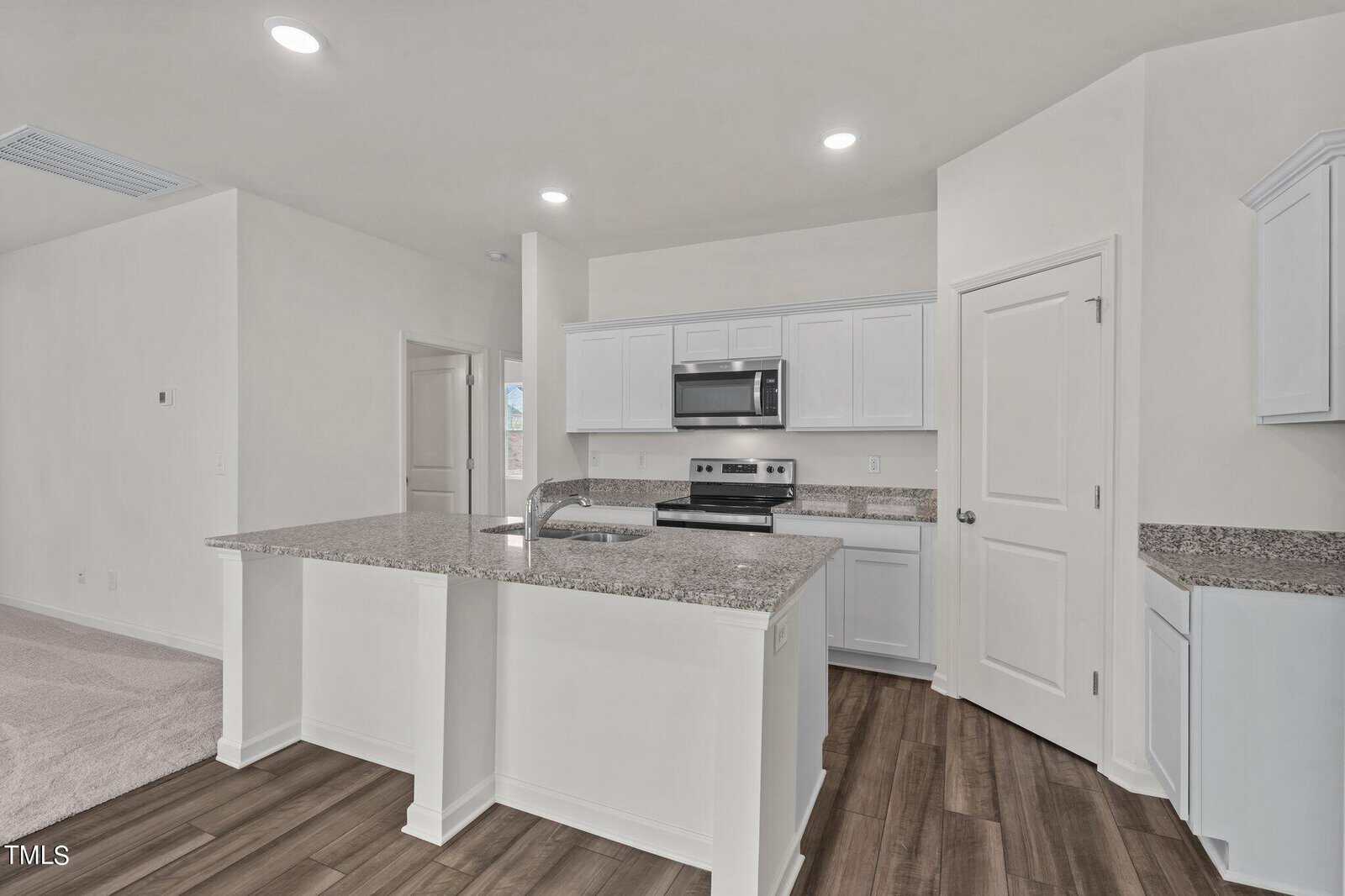 Modern kitchen with white cabinets, stainless steel appliances, granite countertops, a large island with a sink, and wood-style flooring. The space is bright with recessed lighting and an open layout.