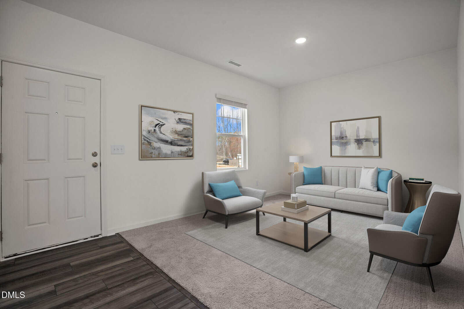 A modern living room with white walls, a window, a white front door, gray couch, two gray chairs with blue pillows, a coffee table, two abstract paintings, and a table lamp on a side table.