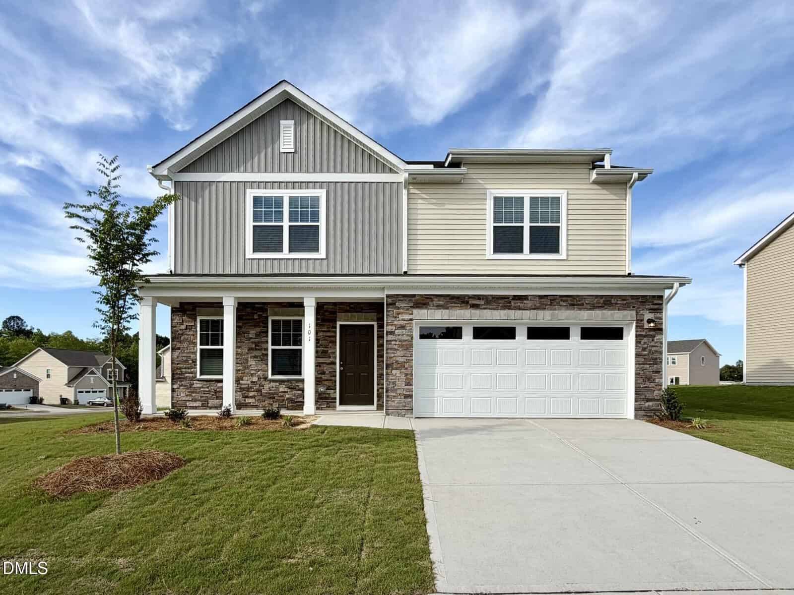 Charming two-story suburban house at 101 Big Dream Court, Louisburg, featuring a double garage, beige siding, stone accents, white trim, and a covered front porch. Enjoy a lush lawn, young tree, and concrete driveway under blue skies with clouds.