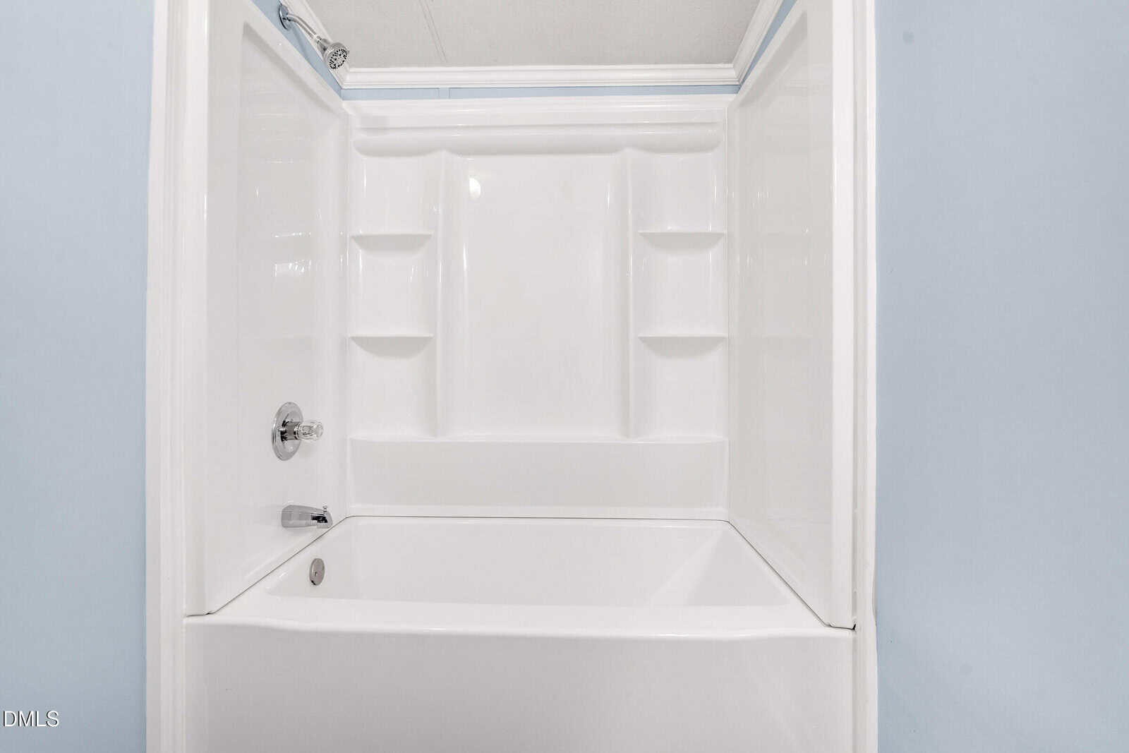 A white bathtub and shower combination with built-in shelves on three sides, chrome faucet and showerhead, and light blue walls.