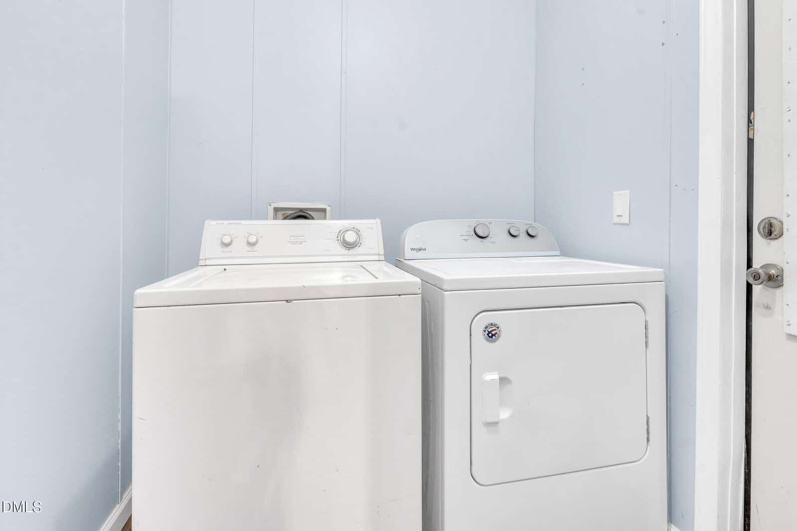 A white top-loading washing machine and a white front-loading dryer are positioned side by side in a small laundry room with light blue walls.