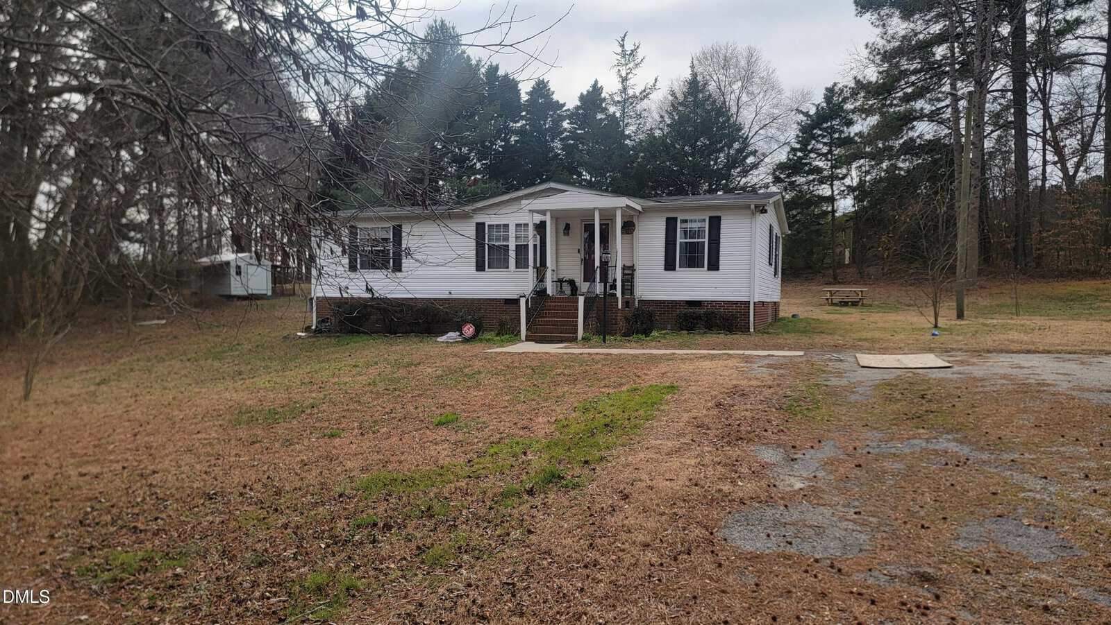 A single-story white house with black shutters and a covered front porch stands on a large grassy lot at 5154 Dorsey Road, Oxford, with scattered trees in the background and a driveway in the foreground.