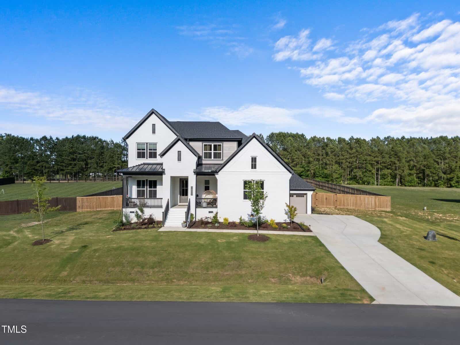 Located at 105 Scotland Drive in Youngsville, this two-story modern white house features a front porch, attached garage, large driveway, and a spacious lawn bordered by trees under a partly cloudy blue sky.