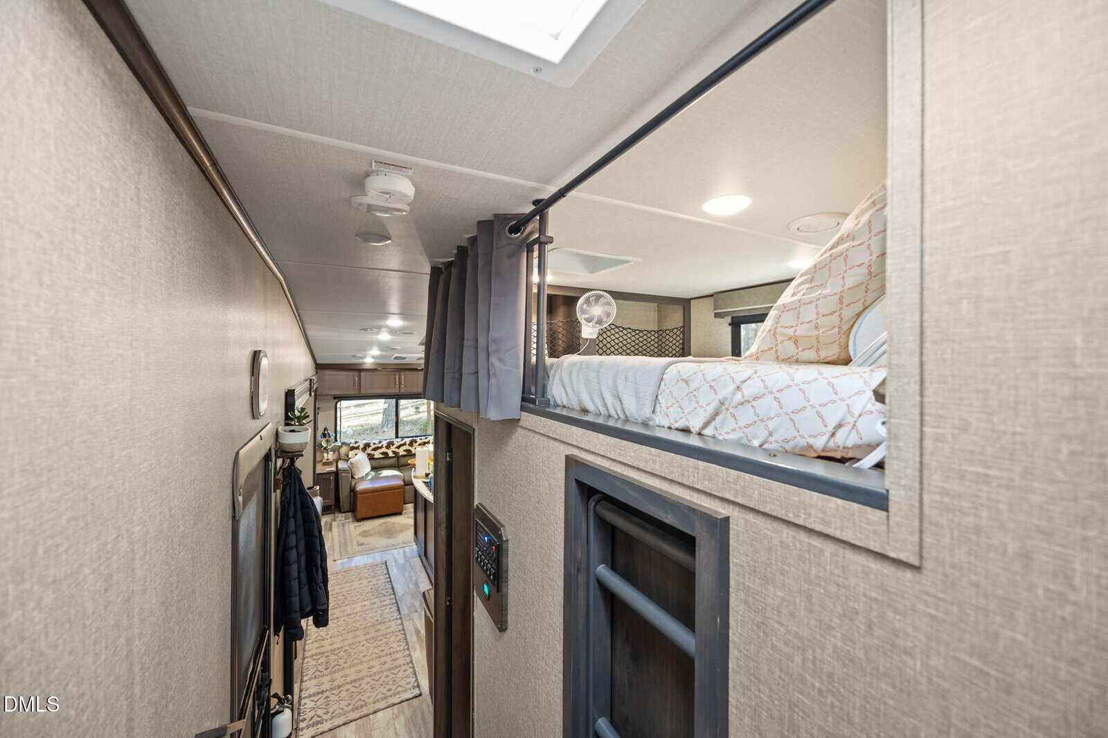 Interior view of an RV featuring a hallway with a ladder leading to a lofted bed, a curtain for privacy, and a living area with seating and decor visible toward the back.