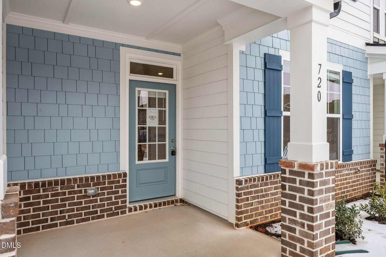 A covered front porch with light blue siding, a matching blue door with glass panels, white trim, dark blue shutters, brick accents, and the house number 720 on a white column.