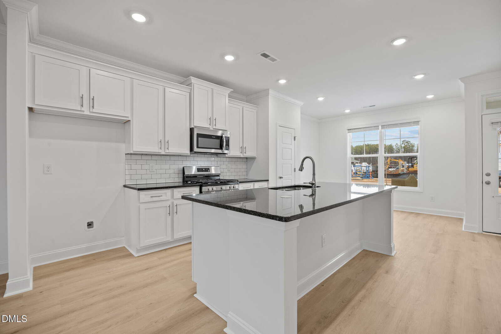 Modern kitchen with white cabinets, stainless steel appliances, a subway tile backsplash, and a large island with a black countertop. Light wood flooring and large windows provide natural light.