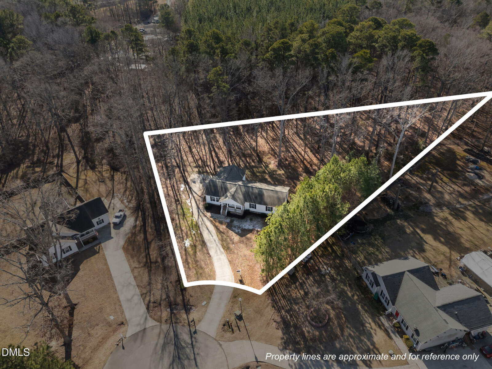 Aerial view of a triangular property outlined in white, featuring a house surrounded by trees and neighboring homes, with a curved driveway leading to the property. Text notes property lines are approximate.
