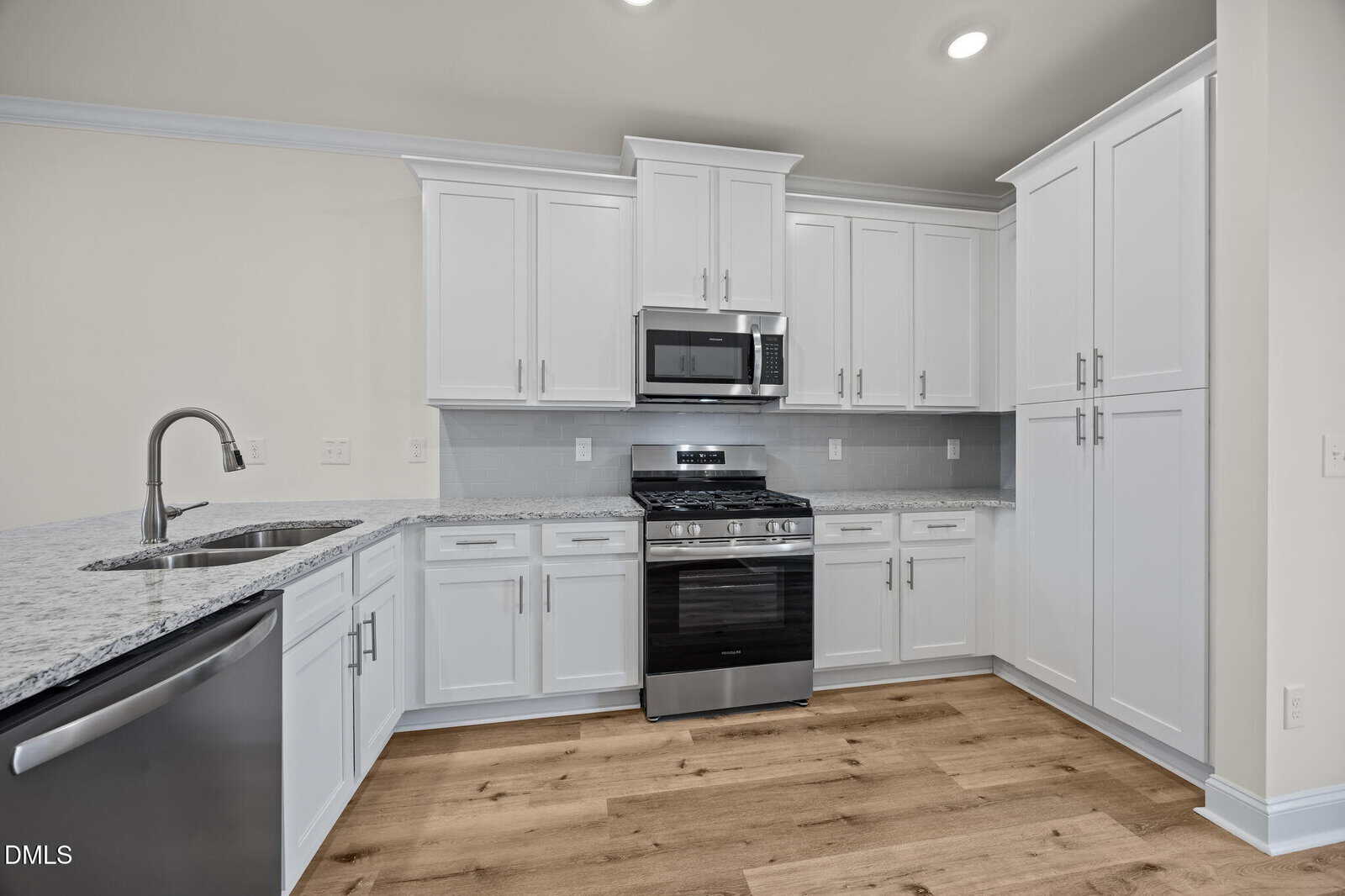 Modern kitchen with white cabinets, stainless steel appliances, gas stove, microwave, dishwasher, marble countertops, and light wood flooring. The space is clean, bright, and features under-cabinet lighting.