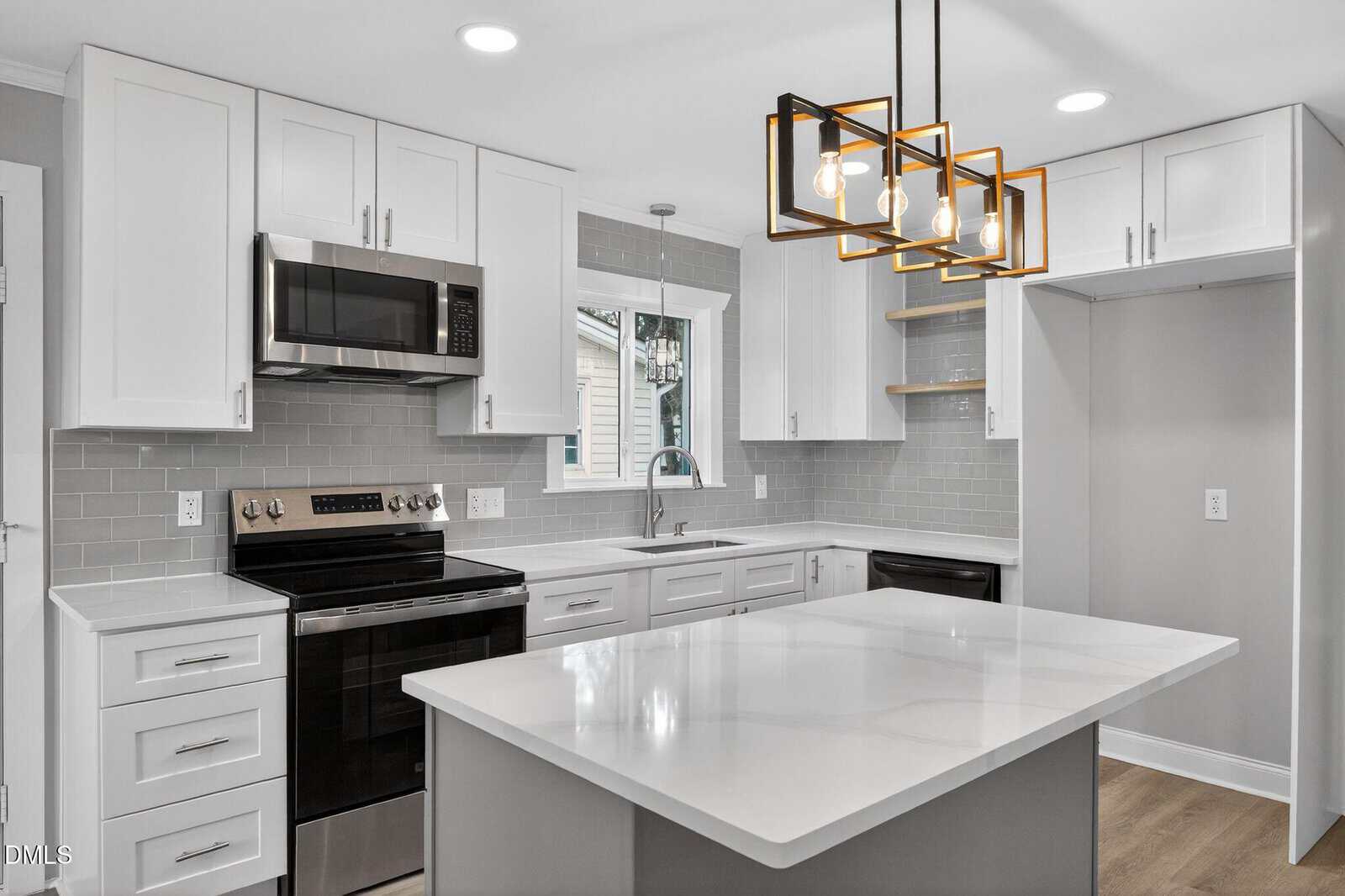 Modern kitchen with white cabinets, gray subway tile backsplash, stainless steel appliances, an island with a white countertop, and a geometric pendant light fixture. A window is above the sink.