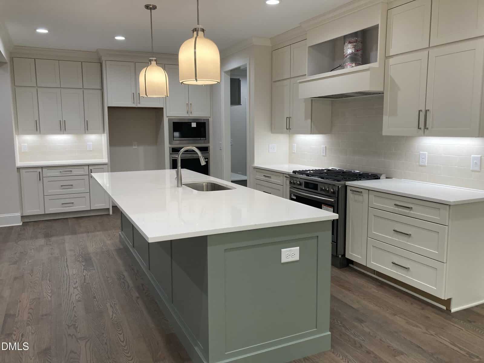 A modern kitchen with light wood floors, white cabinetry, a large island with a sink, stainless steel appliances, two pendant lights above the island, and neutral tile backsplash.