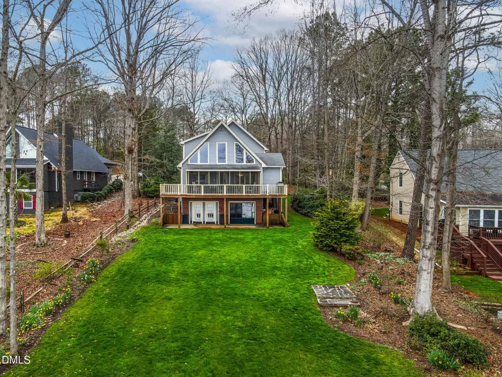 Situated at 651 Sagamore Drive in Louisburg, this two-story gray house with large windows and a wooden deck overlooks a spacious, well-maintained green lawn, surrounded by trees and neighboring homes on either side.
