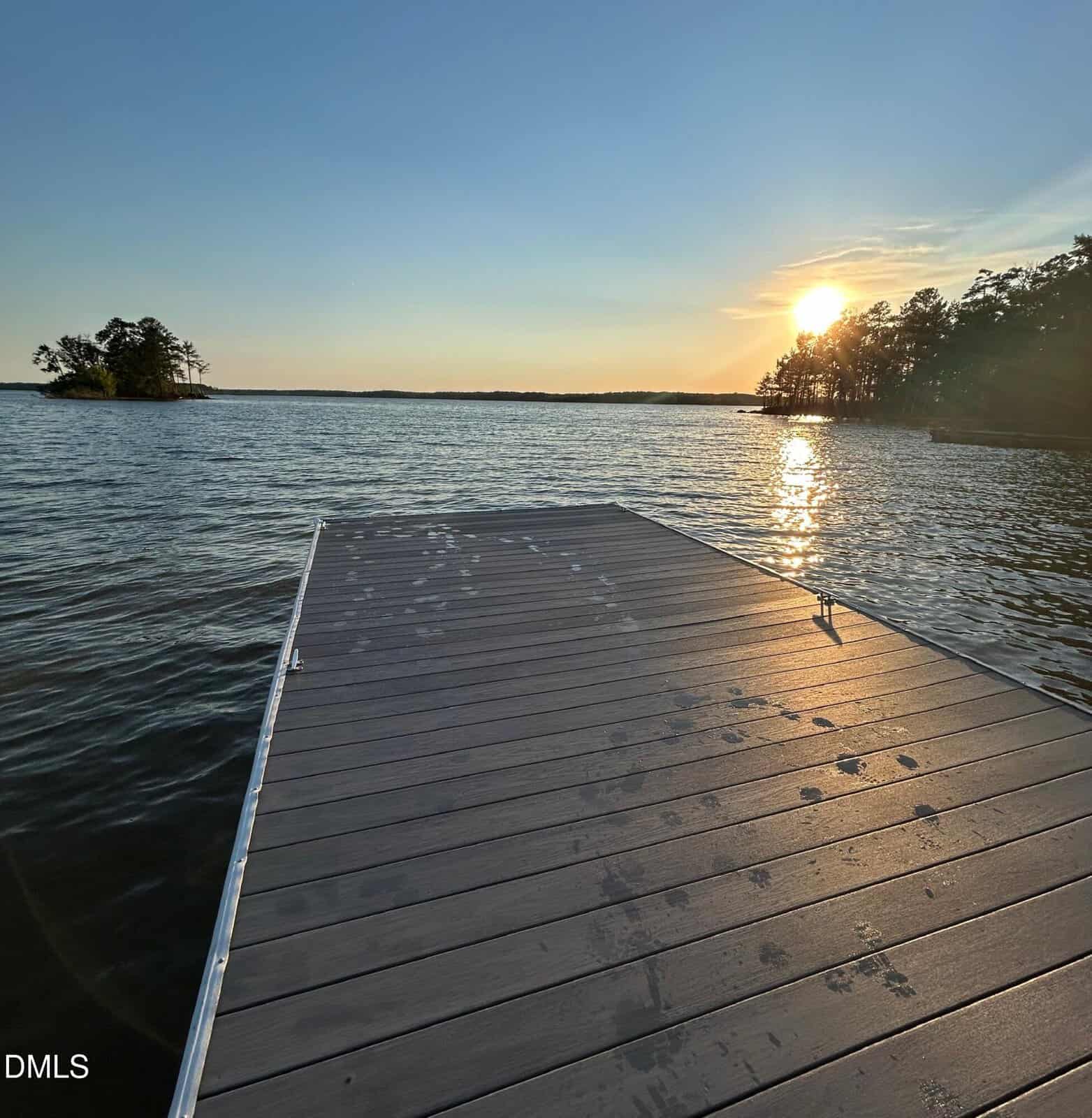 A wooden dock at 317 Doc Lane extends over a calm Manson lake at sunset, with golden reflections on the water; trees line the shore and a small island is visible in the distance.