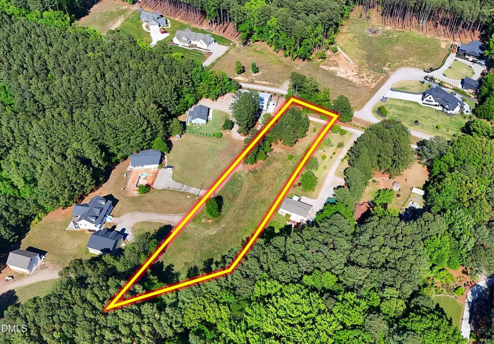 Aerial view of a residential area with a triangular plot of land outlined in orange, surrounded by trees and houses on a curving road.