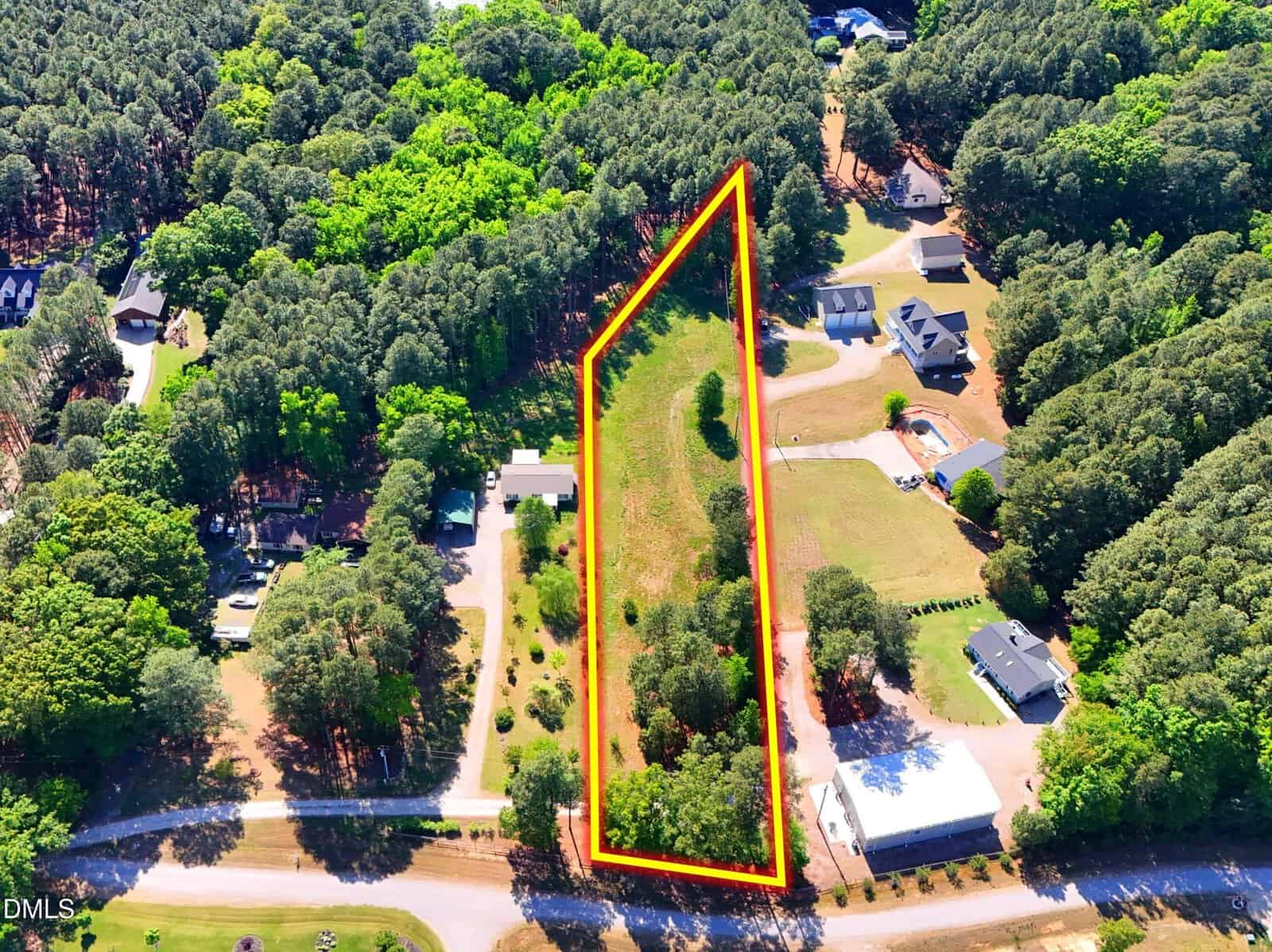 Aerial view of a rectangular plot of land outlined in red, surrounded by trees and neighboring houses in a suburban area, with a road running along the front of the property.