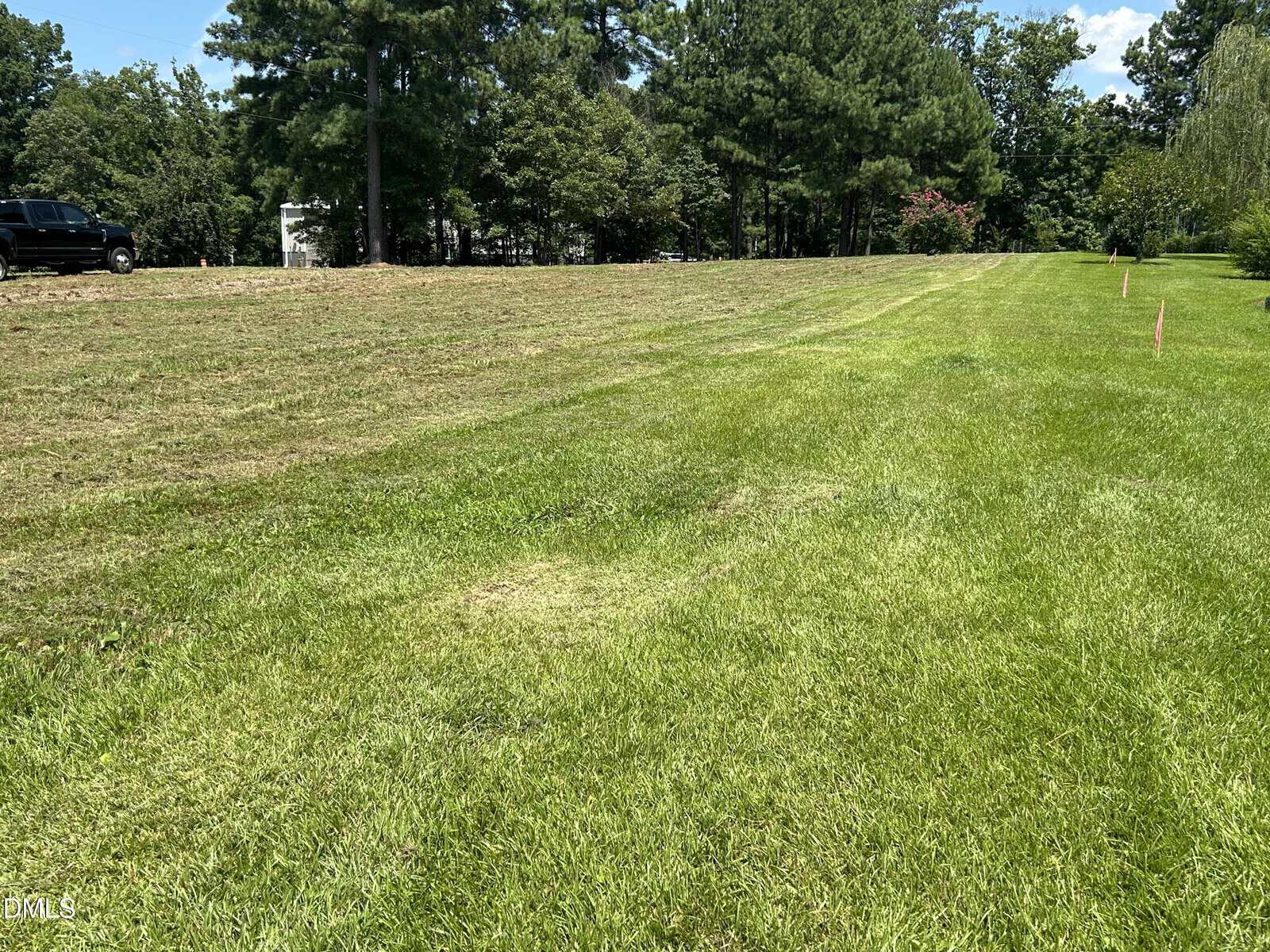 A mowed grassy field with trees in the background, a parked black truck on the left, and pink markers along the right side under a sunny blue sky.