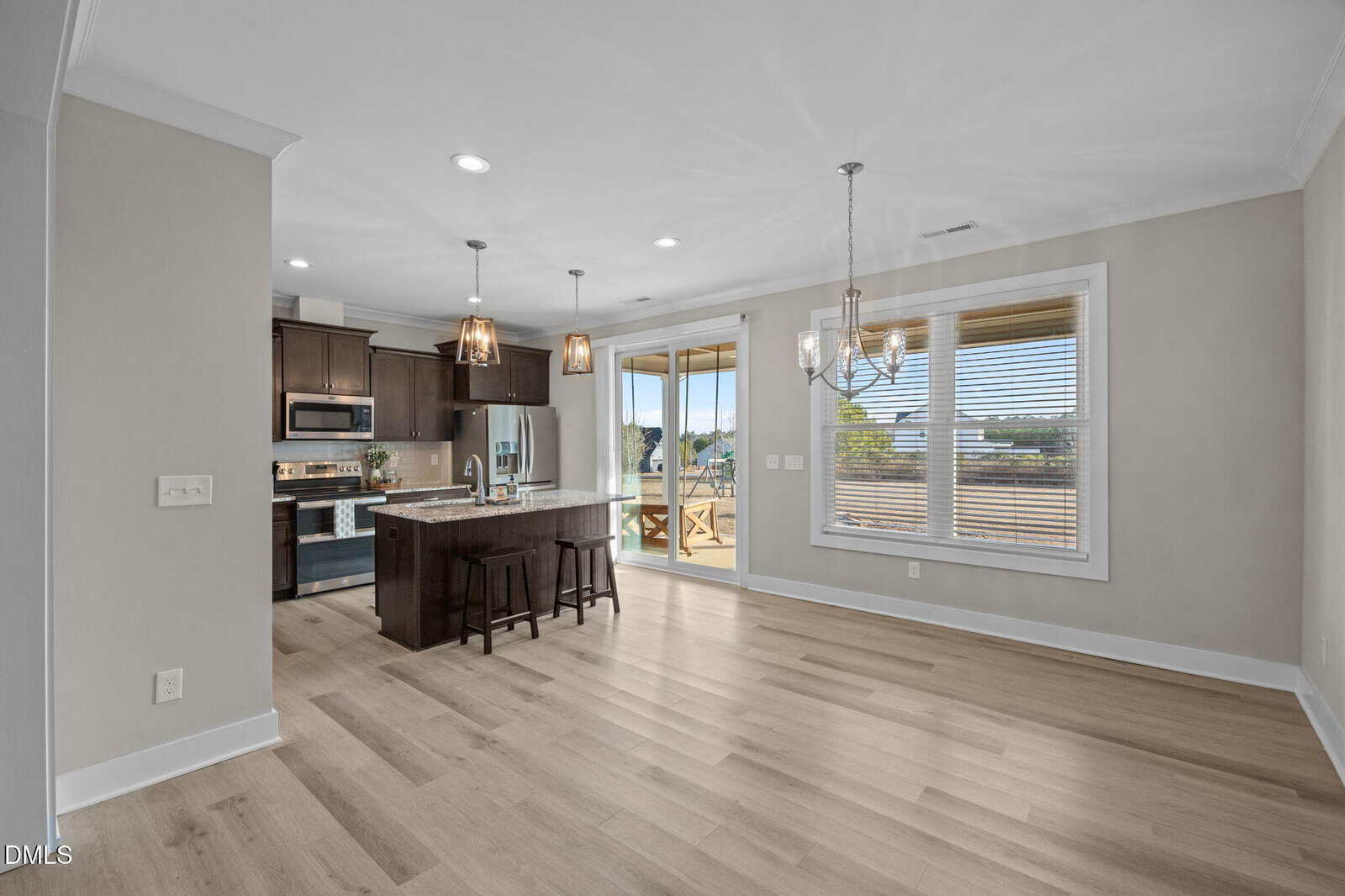 Modern open-concept kitchen and dining area with wood floors, dark island, stainless steel appliances, pendant lights, large window, and sliding doors leading to a deck with scenic views.