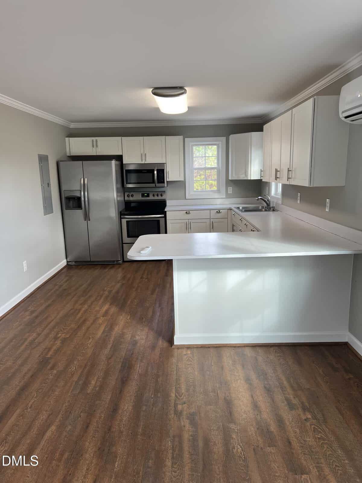 Modern kitchen with white cabinets, stainless steel appliances, and wood-look flooring. A large countertop with a breakfast bar extends into the room, and a window lets in natural light above the sink.