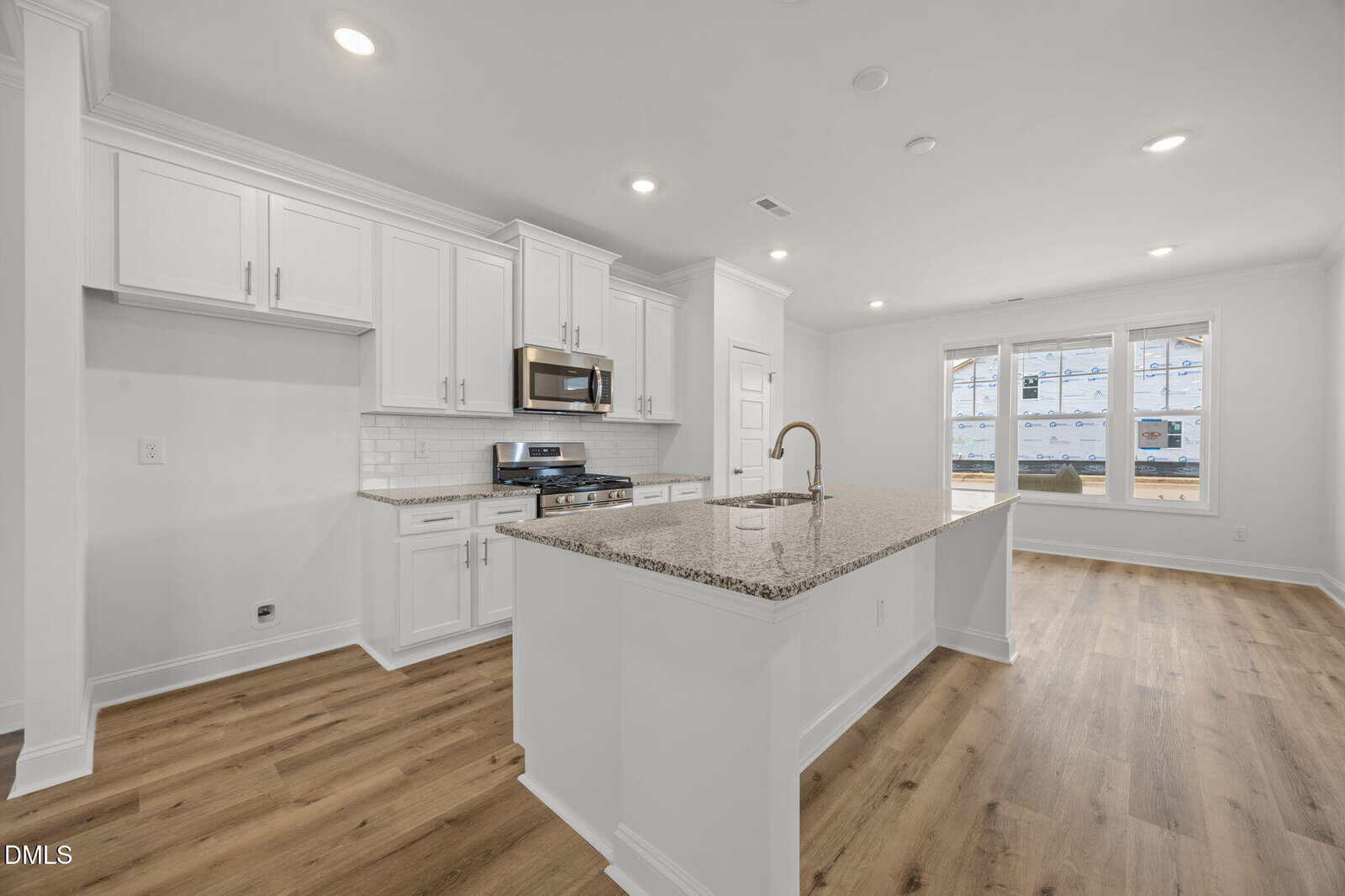 Modern kitchen with white cabinets, stainless steel appliances, granite island with sink, wood flooring, recessed lighting, and large windows letting in natural light.
