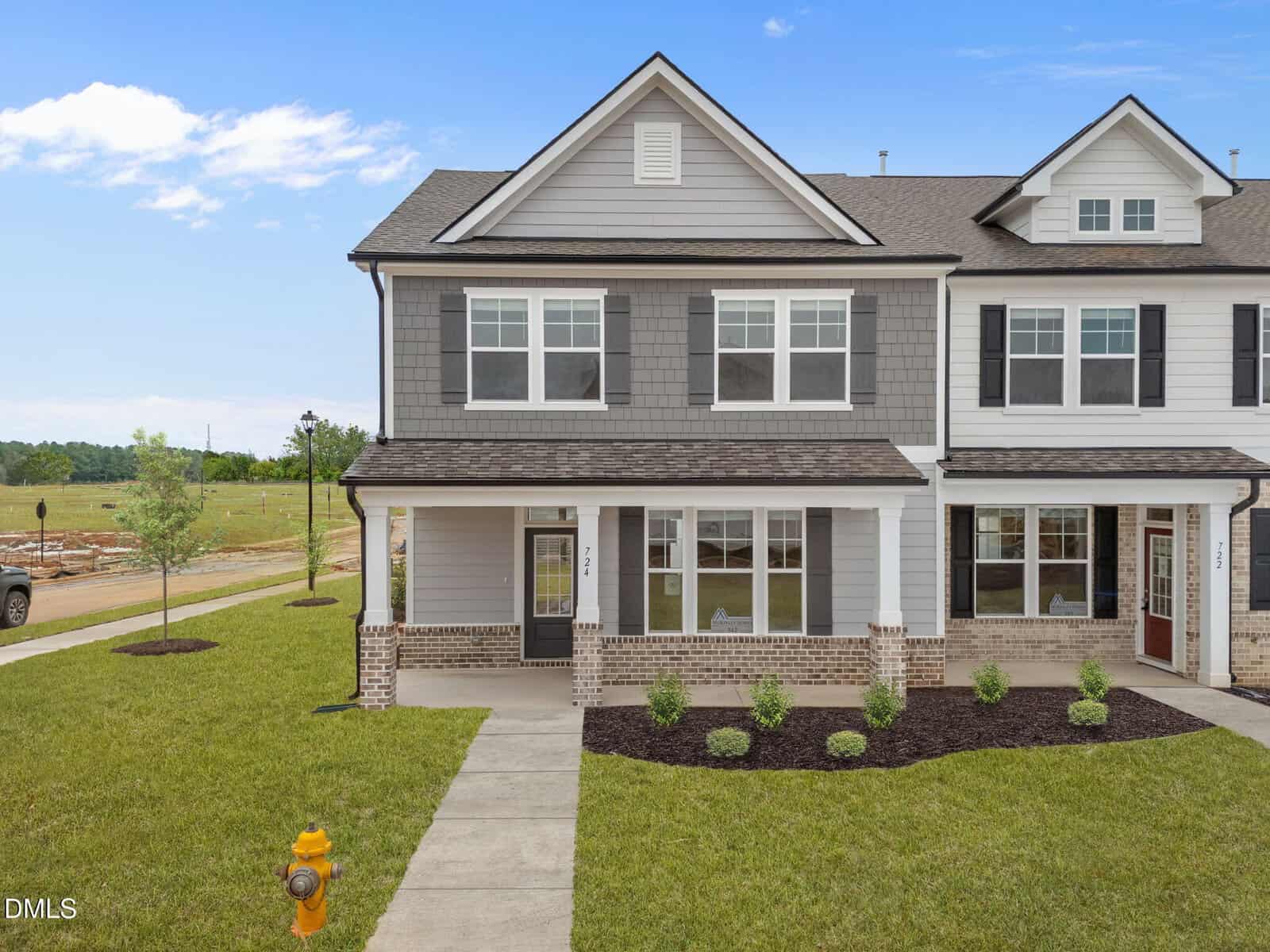 Two-story townhouse with gray and white siding, large front windows, and a covered porch. Manicured lawn and shrubs in front, a yellow fire hydrant near the sidewalk, and open green space in the background.