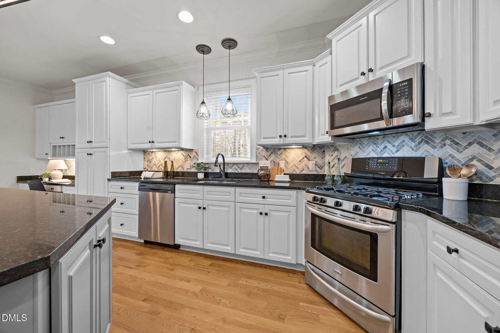 Modern kitchen with white cabinets, stainless steel appliances, black granite countertops, and a chevron-patterned backsplash. There are pendant lights over the sink and hardwood floors throughout the space.