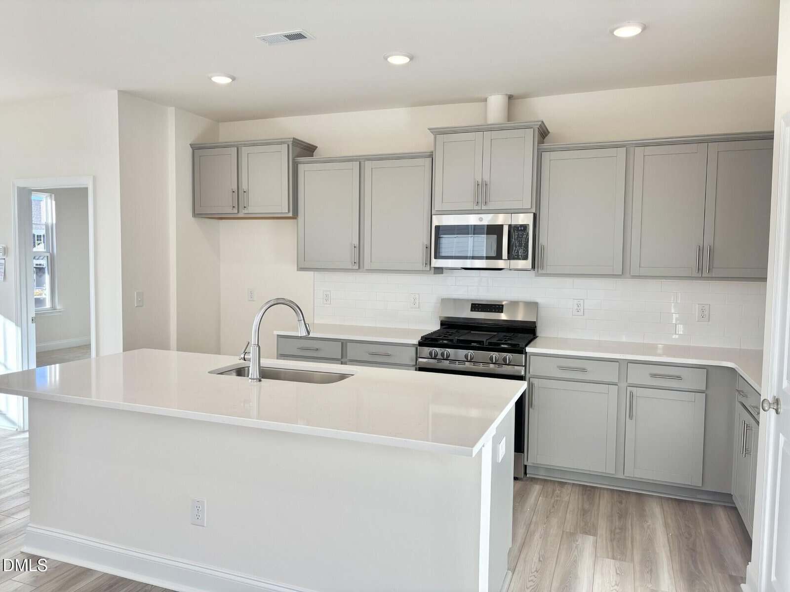 Modern kitchen at 10 Gerrard Street in Franklinton features gray cabinets, stainless steel appliances, built-in microwave, gas stove, white subway tile backsplash, and a large island with sink. Light wood floors and bright lighting throughout.