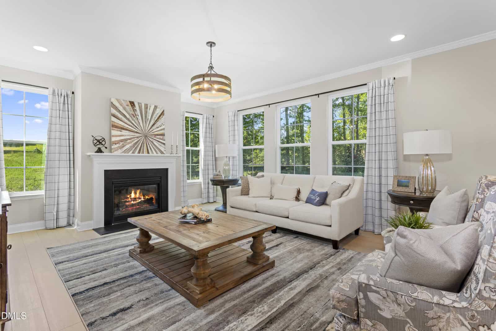 Bright living room at 255 Sugar Pine Drive in Franklinton with large windows, beige walls, a fireplace with art above it, a cream sofa, an armchair with a patterned pillow, wooden coffee table, and striped rug on light wood floors.