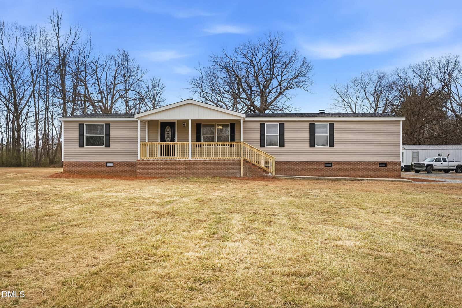 A single-story manufactured home in Oxford at 3508 Windwood Circle features beige siding, a brick foundation, and a front porch with yellow railings, set on a large grassy lot with bare trees and a white pickup truck in the background.