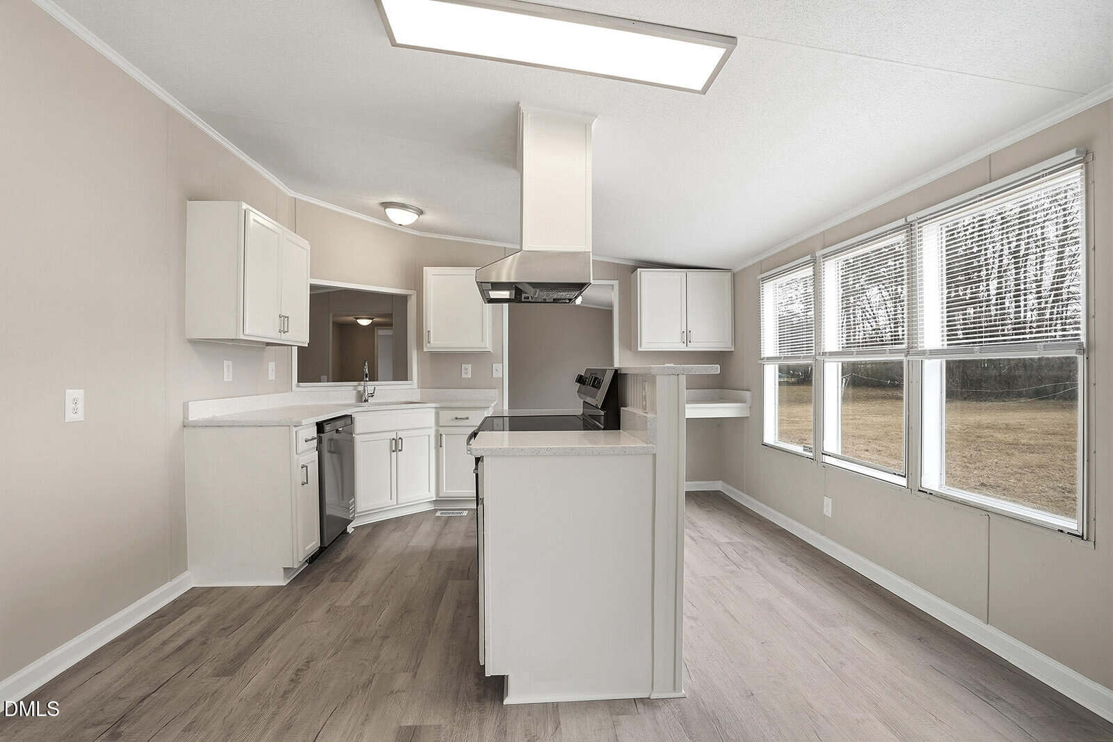 Modern kitchen with white cabinets, stainless steel appliances, an island cooktop, and large windows letting in natural light. Light wood flooring and neutral walls create a bright, open space.