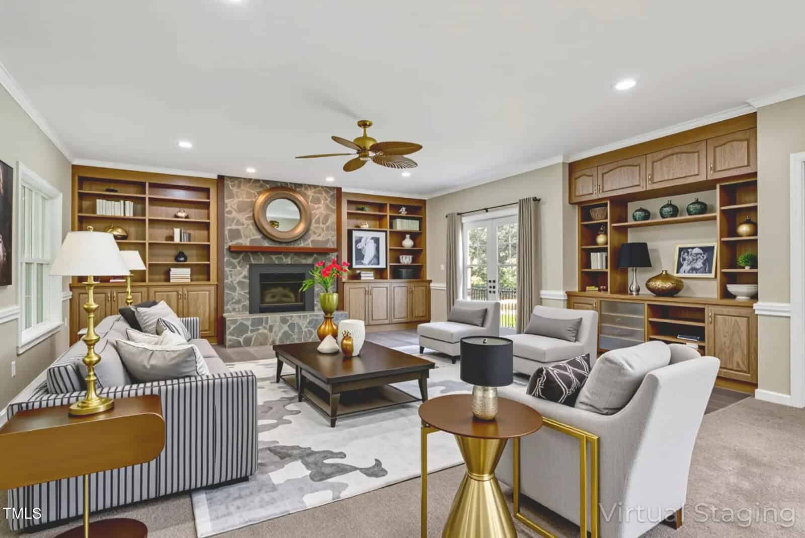 A spacious living room with built-in wooden shelves, a stone fireplace, and several gray and beige sofas and chairs arranged around a large dark coffee table. Windows and glass doors let in natural light.