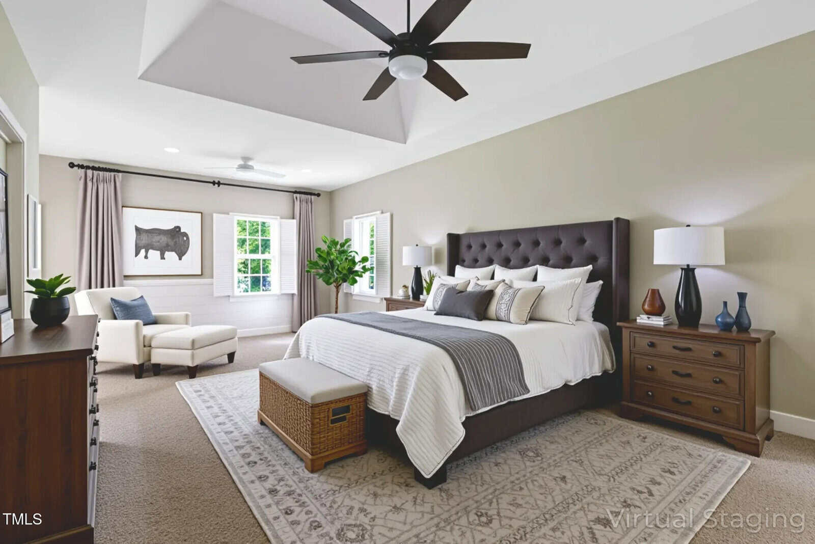 A spacious, modern bedroom with a large bed, two wooden nightstands, a bench at the foot of the bed, an armchair by the window, a dresser, a ceiling fan, and neutral decor with natural light.