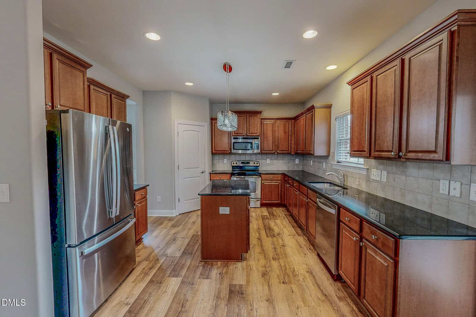 Modern kitchen with wooden cabinets, stainless steel appliances, a center island, black countertops, tile backsplash, hardwood floors, recessed lighting, and a window above the sink.