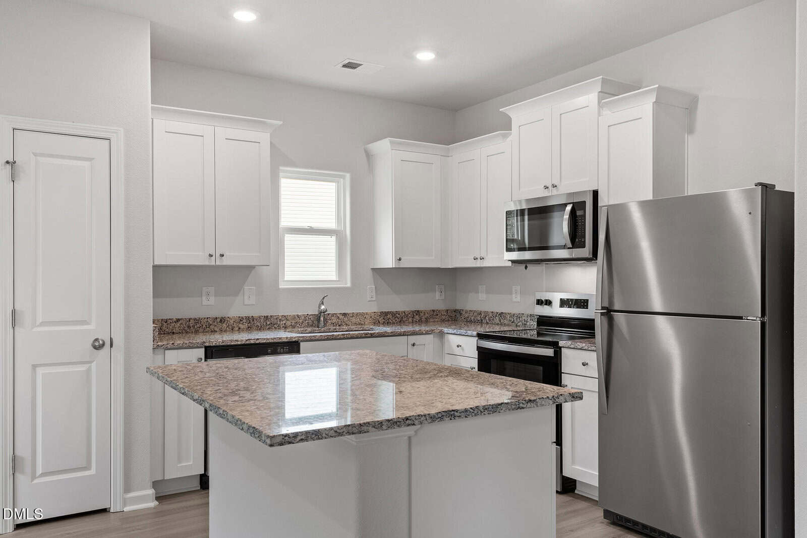 A modern kitchen features white cabinets, stainless steel appliances, granite countertops, an island in the center, a small window above the sink, and recessed lighting in the ceiling.