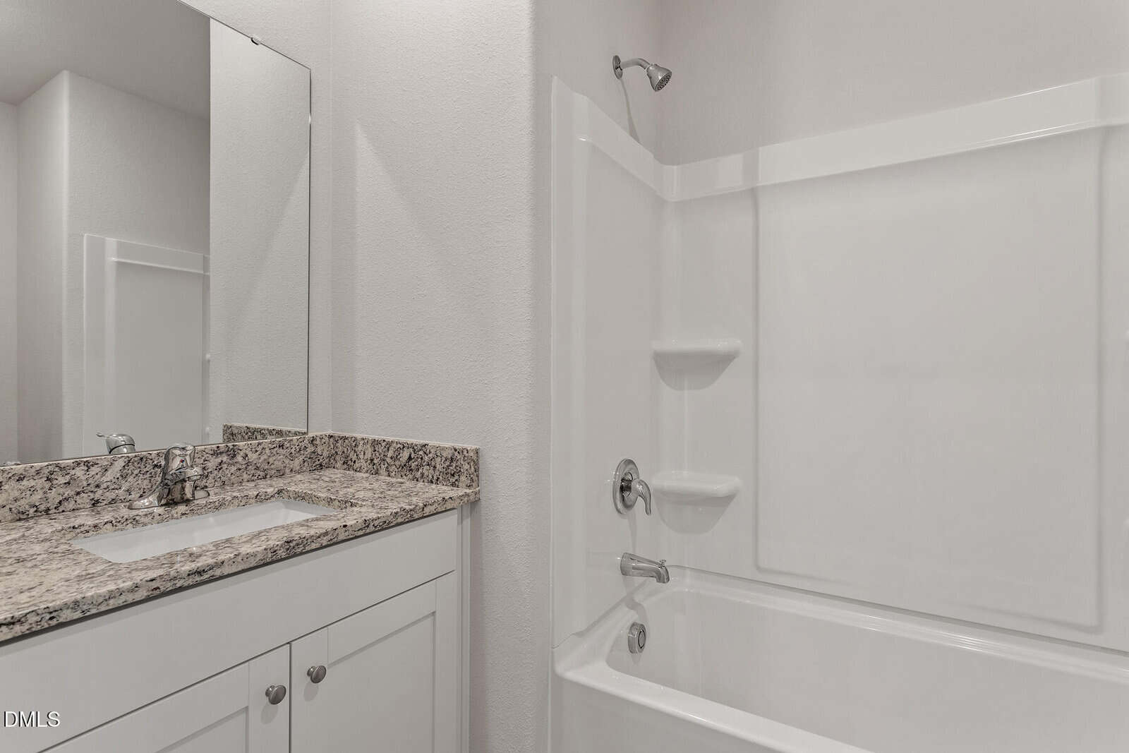 Modern bathroom with a granite countertop vanity, white cabinets, and a white bathtub-shower combo with built-in corner shelves, all against light-colored walls.