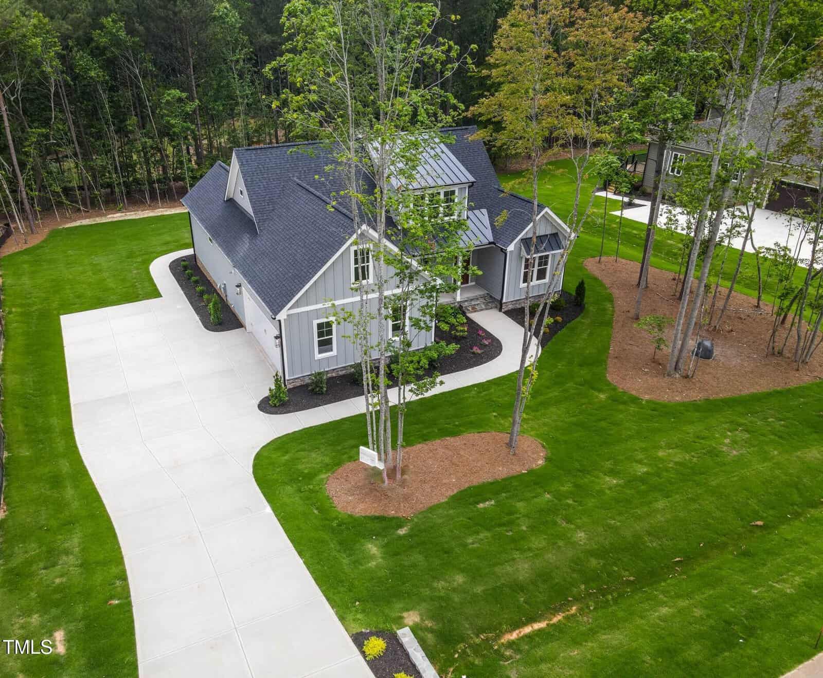 Aerial view of a gray, single-story house at 3909 Cedar Knolls Drive in Youngsville, with a dark roof, green lawn, trees, and landscaped mulch beds. A curved white driveway leads to the front-facing garage and entryway.