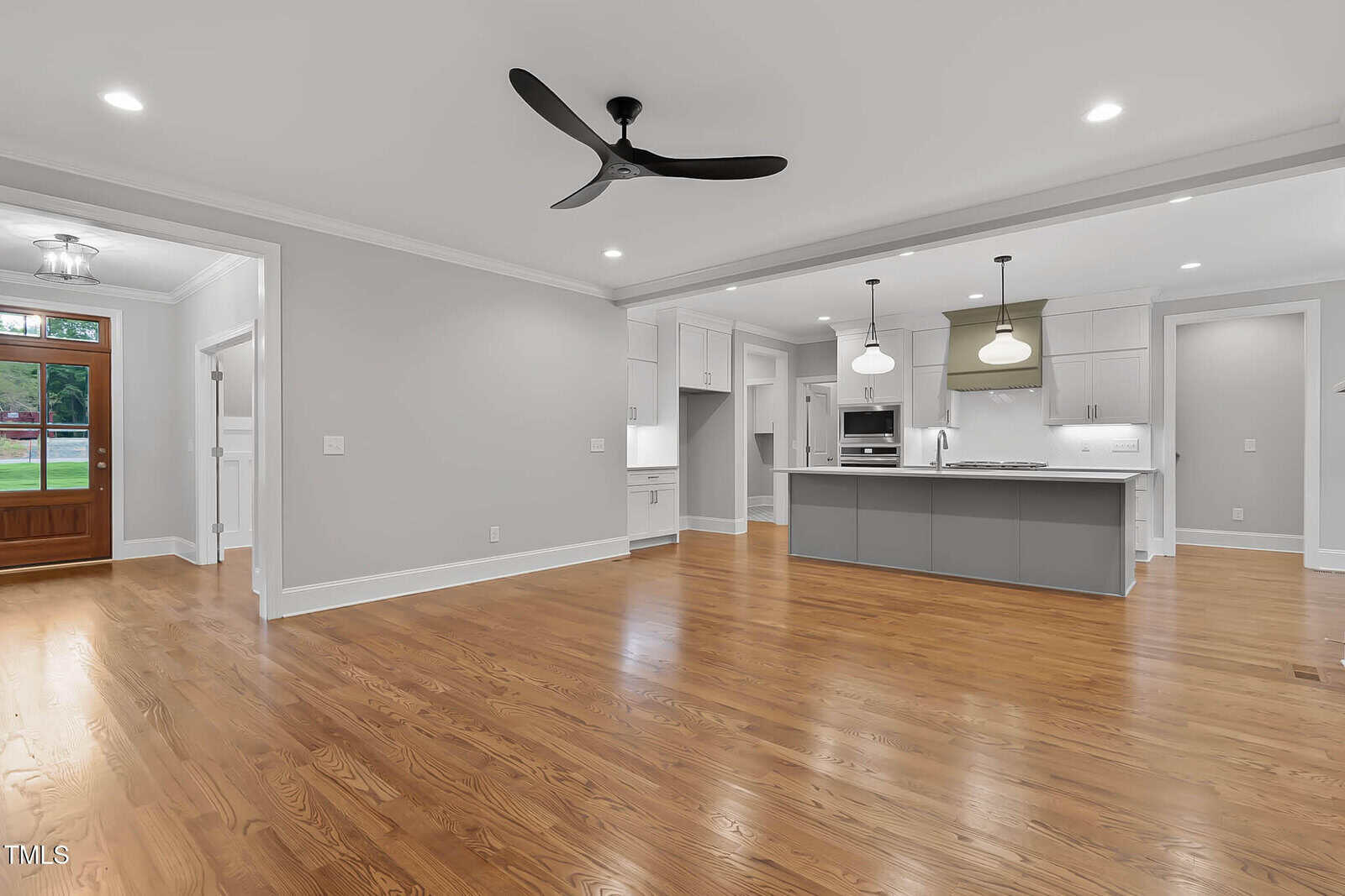 Spacious open-concept living area with hardwood floors, ceiling fan, recessed lighting, modern kitchen with island, pendant lights, and a wooden front door with glass panels.