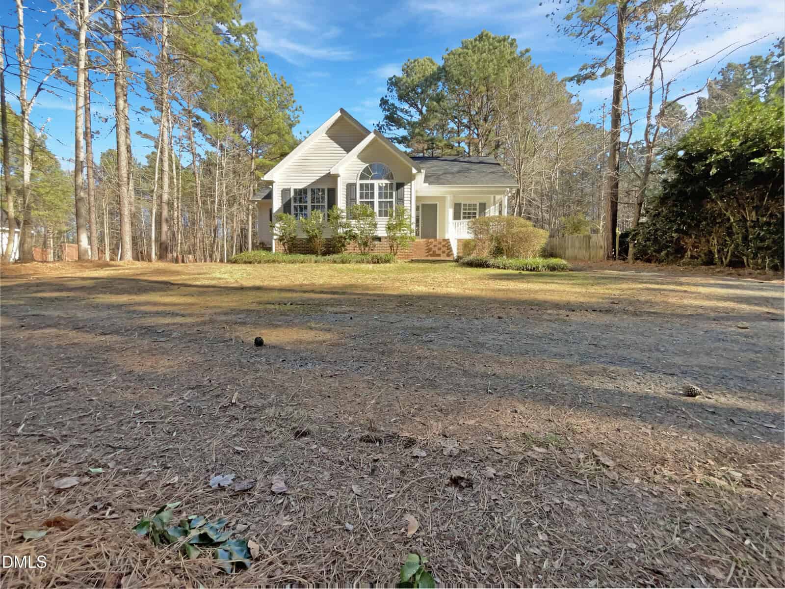 A single-story white house at 4054 Brooksdale Drive, Franklinton, sits in the center of a large yard covered with pine needles, surrounded by tall pine trees under a blue sky.