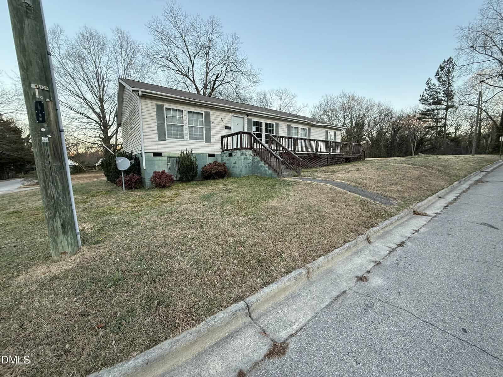 A single-story beige house with a wooden ramp-style front porch sits on a grassy corner lot at 603 Arch Street in Henderson. Leafless trees dot the yard, and a utility pole stands near the street in the foreground.